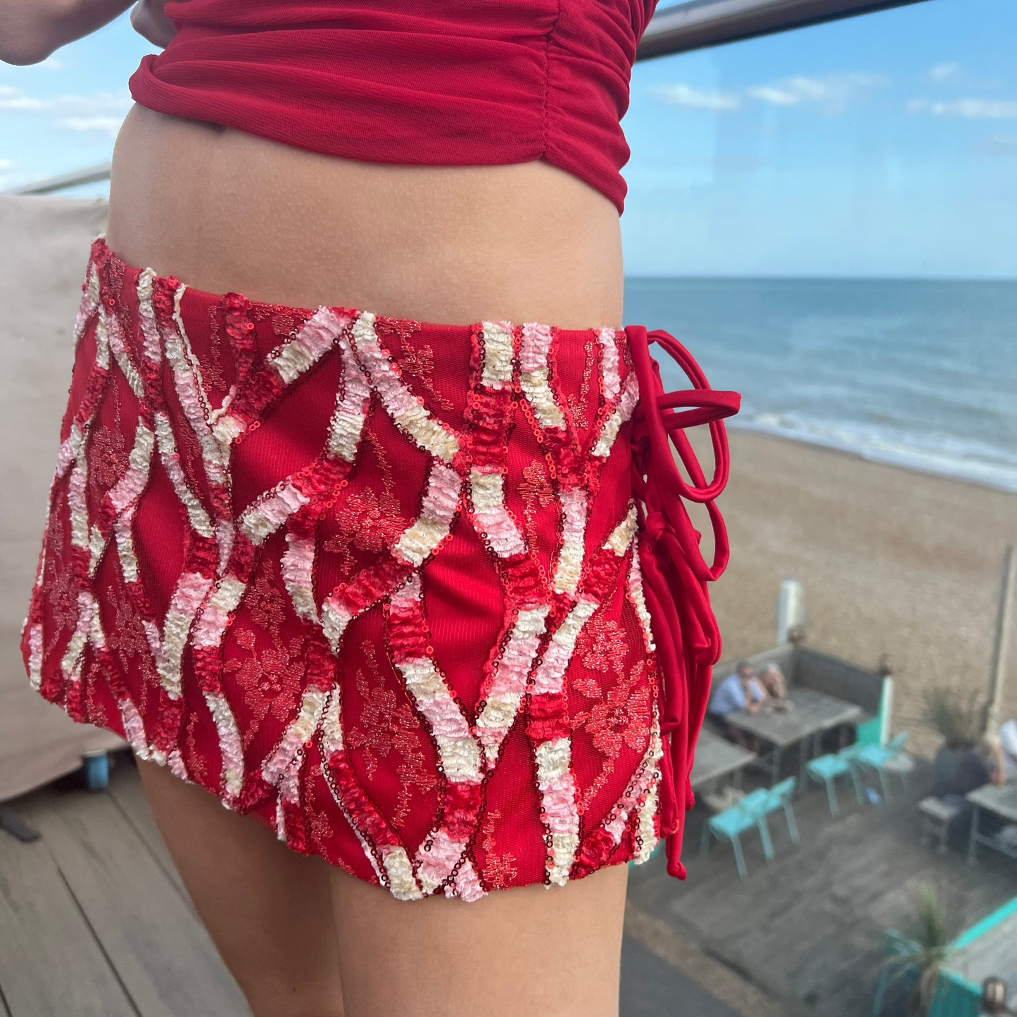 Person wearing a red patterned skirt on a beach with ocean view